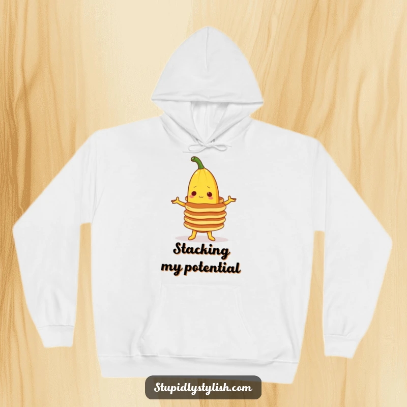 Funny hoodie featuring a banana character precariously balancing a stack of pancakes, offering warm comfort and breakfast-themed amusement.